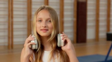 Kafkasyalı neşeli küçük kız kulaklık takıyor müzik şarkısı dinliyor mutlu çocuk çocuk beden eğitimi öğrencisi gülümseyen cihaz dansçısı öğrenci spor eğitimi alıyor.