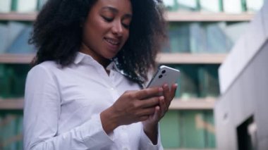 Afro-Amerikalı kadın iş kadını gülümseyen iş kadını cep telefonu teknolojisi kullanıyor çevrimiçi bağlantı kuruyor, mesajlaşıyorlar, güler yüzlü şehir e-posta işi dışında.