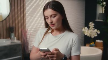 Beyaz kadın ev sahibi. Ev banyosunda alet kullanıyor. Gülümsüyor. Cep telefonu numarası yazıyor.