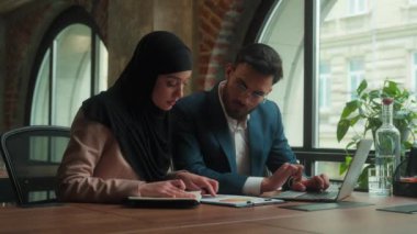 İki iş ortağı, çok ırklı Arap Müslüman iş arkadaşları, ofiste birlikte çalışıyorlar. Belgeleri analiz ediyorlar. Kadın, kadın, erkek, iş kadını, tesettürlü notlar yazıyorlar.