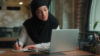 Müslüman Arap İslami kız tesettürlü gülümseyen kadın iş kadını kadın dizüstü bilgisayar video görüşmeleri kağıt dökümanına işaret ederek online çatışma rapor satış grafiği iş sunumunu tartıştı