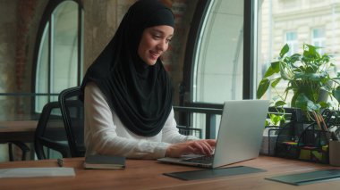 Kadın tesettürlü Müslüman kadın, Arap serbest işçi, iş kadını, ofis müdürü, bilgisayarlı, gülümseyen İslamcı iş kadını, iş yerindeki bilgisayarlı bilgisayarla uzaktan kumandalı iş kadını.