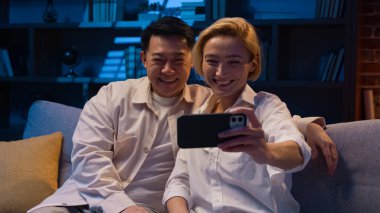 Mutlu, çoklu etnik çeşitlilikte bir çift, çeşitli Asyalı ve Kafkasyalı bir adamla evlendi. Video konferansı yapıyorlar. Cep telefonu uygulaması konuşmaları, geceleri kanepe kanepesinde el sallıyor.