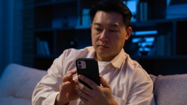 Gece vakti Asyalı orta yaşlı bir adam evinde cep telefonu uygulamasını kaydırıyor. Cihaz bağımlısı Koreli erkek akıllı telefon alışverişi yapıyor. İnternetten sosyal medyada geziniyor ve gece vakti cep telefonuyla sohbet ediyor.