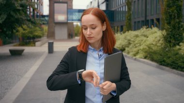 Kafkasyalı iş kadını buluşma saatini bekliyor. Kol saatine bakıyor. İş kadını şehir dışında, ofis binasının yanında bekliyor.