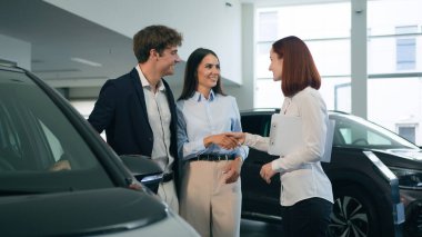 Kafkasyalı çift müşterileri anlaşma anlaşmasını sonuçlandırdı. Galeri kiralama hizmetlerinde yeni otomobil satın alıyorlar. Kira nakliyesi kadın tüccar tüccar satıcısıyla el sıkışıyor.