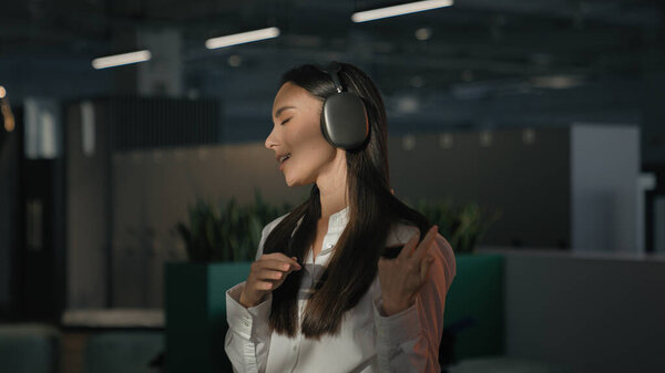 Inspired Caucasian businesswoman employer office worker business woman girl manager indoors at workplace listening music in earphones headphones listen audio sing singing song enjoy break work pause
