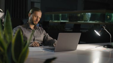 Gece fazla mesai yapan iş adamı. Karanlık ofis laptopuyla çalışıyor. Ciddi bir iş adamı şirket lideri.