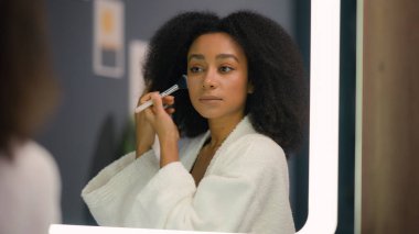 Kadın aynası yansıması güzellik makyaj konsepti çift ırklı güzel Afro-Amerikalı kadın banyo evinde cilt bakımı için pudra sür makyaj malzemesi hazırla