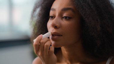 Afro-Amerikan kadın makyajı doğal pürüzsüz nemlendirici ruj, çift ırklı kadın, dudak kremi, cilt bakımı, nemlendirici, kozmetik ürün dudak parlatıcısı sürüyor.