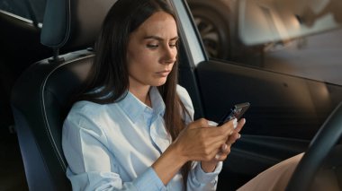 Endişeli, endişeli, beyaz kadın şoför, arabada oturan iş kadını. Araba içinde hayal kırıklığına uğramış, elinde cep telefonu tutmakta. İş sorunu, kötü haber, stres mesajı.