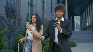 İki iş arkadaşı zımbırtısı Arap iş kadını havaalanı terminalinde cep telefonu kullanıyor. Hintli işadamı, bavul valizli akıllı telefona göz atıyor.