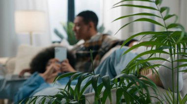 Kanepede oturan Afro-Amerikan çift koca serbest çalışan erkek arkadaş bilgisayarlı uzaktan kumandalı kadınla çalışan kız arkadaş cep telefonu uygulaması, sosyal medya, kanepe mutlu aile.