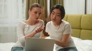 İki mutlu çok ırklı arkadaş çok ırklı kadın çeşitliliği kadın Kafkas Asyalı Japon Çinli yatak odası alışverişi internetten mobilya satın alın dizüstü bilgisayarlı e-ticaret tartışması