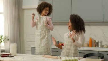 Mutlu Afro-Amerikan aile kadını kadın anne birlikte mutfakta eğleniyor küçük kız çocuk kız çocuk önlüklerle dans ediyor yemek pişiriyor, dinleniyor hafta sonu eğlencesini taşıyor.