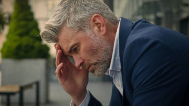 Düşünceli, orta yaşlı, düşünceli, üzgün, tedirgin, kıdemli iş adamının baş ağrısı, migren ağrısı, kariyer başarısızlığı, açık havada yetişkin bir iş adamını iflasa sürükledi.