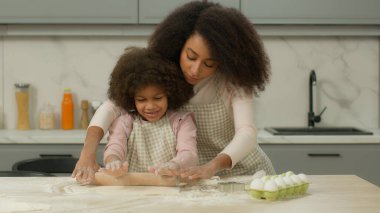 Afro-amerikan mutfağında birlikte yemek pişiren anne un hamurunu düzleştiren annenin, küçük kızına kurabiye pişiren pizzayı nasıl öğrettiğini gösteriyor.