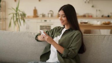 Mutlu gülümseyen kullanıcı kendi evinde rahatlamış gülümseme olumlu memnun Hintli kadın Arap bayan cep telefonu tutan akıllı telefon alışverişi online sohbet uygulaması internet mesajı