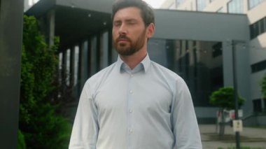 Kafkasyalı, orta yaşlı, düşünceli, düşünceli, düşünceli, erkek, işveren, işveren, iş adamı, şehir binasında karşıdan karşıya geçmiş gülümseyen ellerle kameraya doğru dönüyor.