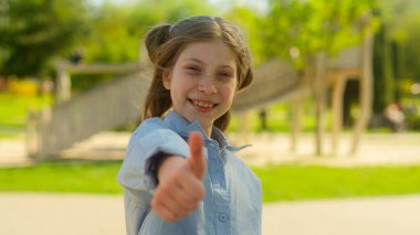 Mutlu genç kız öğrenci öğrenci beyaz çocuk kız evlat edindi kız arkadaş canlısı başparmak göstererek parktaki çocuk parkı sigorta okulunda eğitim gören çocukları tavsiye etti