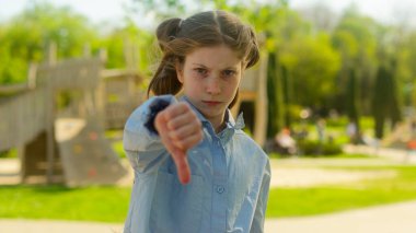 Kafkasyalı kız çocuk çocuk çocuk... ciddi üzgün, tatminsiz liseli kız öğrenci... açık hava parkı öğrencisi... baş parmak hareketi yapıyor... olumsuz zorbalık probleminden hoşlanmadığını göstermiyor.