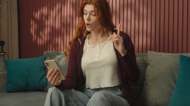 Beyaz kadın, mutlu kız, kullanıcı, ev sahibi, gülümseyen ev sahibi, kanepede uzanan, cep telefonlu sosyal medya bağımlısı, online alışveriş bağımlısı akıllı telefon uygulama hizmetleri.