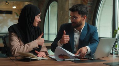 İş arkadaşları Hintli işadamı Arap iş kadını birlikte çalışarak pazarlama kâğıdı grafiklerini analiz ediyorlar. İyi sonuçlar gülümsüyor. Mutlu adam tesettürlü Müslüman kadını onaylıyor.