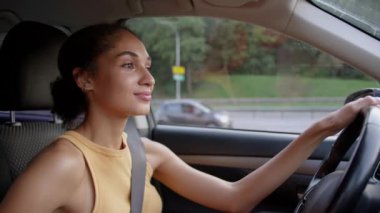 Afro-Amerikalı bir kadın otomobil taşıma aracının içinde araba kullanıyor. Şehirli kadın direksiyoncu, etnik gülümseyen kiralama servisi. Seyahat eden iş kadını.