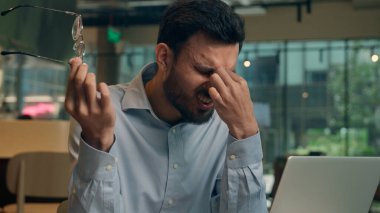 Arap Hintli iş adamı serbest girişimci Kafe çevrimiçi iş bilgisayarı ziyaretçisi yorgun bitkin düşmüş iş adamı yorgun düşmüş gözler zorlanıyor baş ağrısı çekiyor gözlük baş ağrısı baş ağrısı