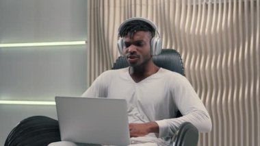 Şaşırtıcı bir şekilde duygusal Afrikalı Amerikalı kaygısız erkek kulaklık takıyor bilgisayar ekranına bakıyor ve 