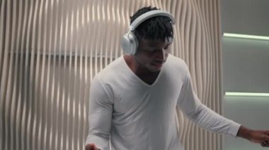 Müzik eşliğinde dans eden Afrikalı Amerikalı erkek kapalı mekanda fütürizm modern iç mekan dansçı erkek kablosuz kulaklıkla dans ediyor fütüristik beyaz stüdyoda müzik sesi dans ritmi dinliyor.