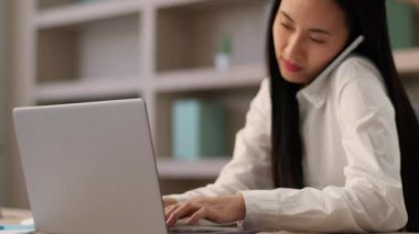 Çok çalışan Asyalı iş kadını Japon iş kadını kız işkadını ofis çalışanı sekreter cep telefonuyla konuşan akıllı telefondan konuşan kapalı bilgisayarlı bilgisayarda çalışan akıllı telefon.