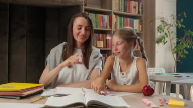 Mutlu Kafkasyalı kadın öğretmen küçük kız öğrenci okulu öğrenme eğitmeni jest şekli gösteren el hareketleri gösteren çocuk öğrencileri fotoğraf çekerken kütüphane parmakları birlikte ders veriyorlar.