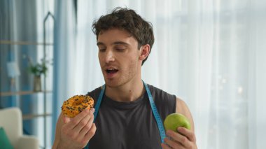 Elmalı donut tutan beyaz bir adam diyet yapmayı tercih ediyor sağlıklı yemekler yiyor sporcu erkek sporcu vejetaryen vitamin vejetaryeni sağlıklı besleniyor doğal fitness kalorisi ısırıyor.