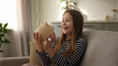 Küçük kız kumbarayı sallıyor para biriktiriyor para yatırıyor yatırım yapıyor çocukluk bütçesi çocuk gülümsüyor keyifle eğleniyor madeni paraların keyfini çıkarıyor sermaye hesabı sermaye fonu sermayesi yatırımı zengin ev