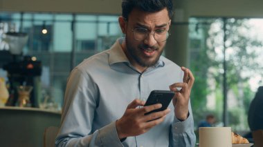 Arap adam etnik müslüman Hintli işadamı girişimci yönetici cep telefonu iş yemeğini kafe restoranında kullanıyor erkek ziyaretçi milenyum turisti mesajları okuyor akıllı telefon mesajları bekliyor