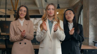 Mutluluktan gülümseyen iş dünyası çoklu etnik çeşitliliğe sahip kadınlar üç çok ırklı iş kadını Koreli Asyalı Kafkasyalı kız alkışları alkışlayarak alkışları destekliyor.