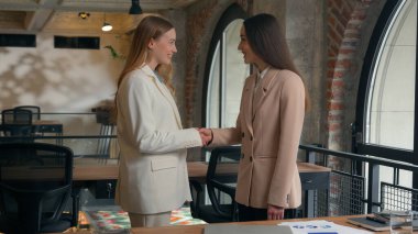 Two happy smiling friendly Caucasian businesswomen girls female business women partners friends coworkers colleagues managers executives in office meeting handshaking greeting talking conversation