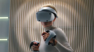 Fütürist neon stüdyo kadını AR aletini keşfediyor yüksek teknoloji VR gözlükler takıyor oyun kaskı simülasyonu kız kız kontrolörlerle sanal arttırılmış video oyunu oynuyor.