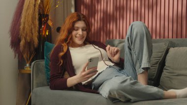 Beyaz kadın, mutlu kız, kullanıcı, ev sahibi, gülümseyen ev sahibi, kanepede uzanan, cep telefonlu sosyal medya bağımlısı, online alışveriş bağımlısı akıllı telefon uygulama hizmetleri.