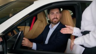 Kafkas erkek müşteri alıcısı yeni otomobili seçiyor. Otomobil test sürüşünün içinde oturuyor. Kadın satıcı kadın kızla banka kredisi hakkında konuşmaya karar veriyor.