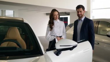 Beyaz kadın satıcı kadın danışman kız. Yeni lüks elektrikli arabayı, müşteri alıcısına gösterme konusunda yardımcı oluyor. Adam, araba satın almayı seçiyor.