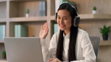 Gülümseyen Asyalı iş kadını Japon Çinli kız iş kadını etnik kadın iş kadını kulaklıklı Koreli ofis çalışanı çevrimiçi video konuşması yapan, bilgisayarlı ev kamerası kullanan.