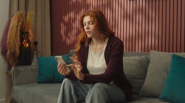 Beyaz kadın, mutlu kız, kullanıcı, ev sahibi, gülümseyen ev sahibi, kanepede uzanan, cep telefonlu sosyal medya bağımlısı, online alışveriş bağımlısı akıllı telefon uygulama hizmetleri.