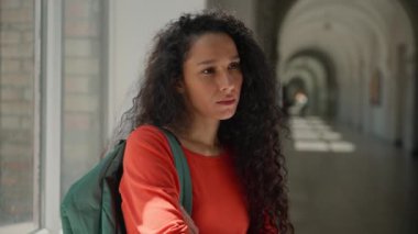 Üzgün, hayal kırıklığına uğramış, üzgün, bunalımlı, düşünceli, Latin bir kadının üniversite akademisi koridorunda öğrenim gördüğünü düşünen, sorunlu, eğitimli, zorbalık yapan Latin bir kız öğrenci.