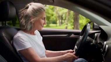 Kafası karışmış yaşlı beyaz kadın büyükanne olgun yaşlı sürücü kadın araba sahibi modern elektrikli otomobilin içinde motorlu araç karışıklığını başlatmaya çalışıyor.