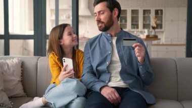 Neşeli Kafkasyalı ebeveyn baba elinde kredi kartı tutan adam finansörden konuşan küçük kız öğrenci kız çocuk cep telefonu e-ticareti yapıyor uzaktan aile kızı baba alışverişi yapıyor.