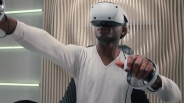 Beyaz fütürizm stüdyosundaki Afrikalı Amerikalı siber adam VR gözlük takan fütürist erkek sanal gerçeklik miğferi 3D alan yenilikçi modern teknolojiyi iş oyunları eğitimi için kullanıyor.