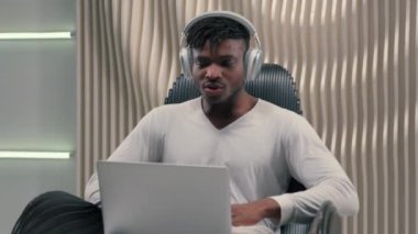 Beyaz fütürizm stüdyosundaki Afro-Amerikan etnik siber adam kapalı mekanda iş adamı erkek kullanıcı hacker iş adamı kulaklıklarda fütüristik adam dizüstü bilgisayar başarısı Bilgisayarda harika haberler elde