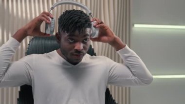 Beyaz fütürizm stüdyosunda Afro-Amerikalı etnik siber adam içeride mutlu parti çocuğu şarkıları söylüyor fütüristik radyo kulaklıkları takıyor dans ediyor müzik şarkıları dinliyor müzik dansı yapıyor